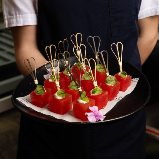 Server presenting watermelon canapés topped with whipped cheese and basil at Two 88 Bar & Kitchen in Sydney CBD.